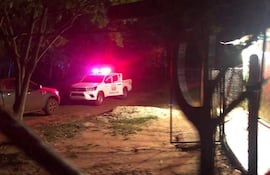 Camioneta de policía con luces intermitentes en un camino de tierra rodeado de árboles, sin personas visibles.