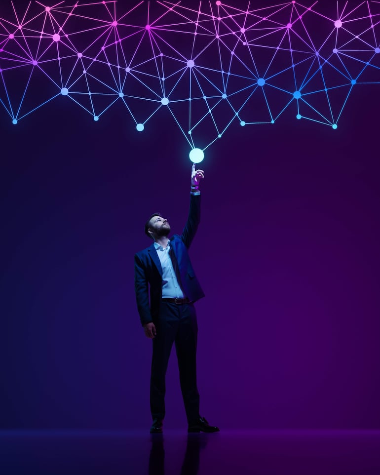 Hombre en traje oscuro y camisa blanca, extiende la mano hacia esfera brillante en fondo azul y morado, simbolizando conexión.