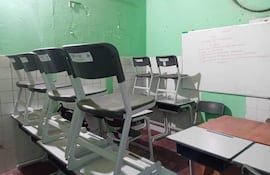 El baño reconvertido en aula. La misma está vacía con sillas apiladas sobre mesas y pizarra blanca. En las paredes se ven aún los azulejos del sanitario desmantelado.