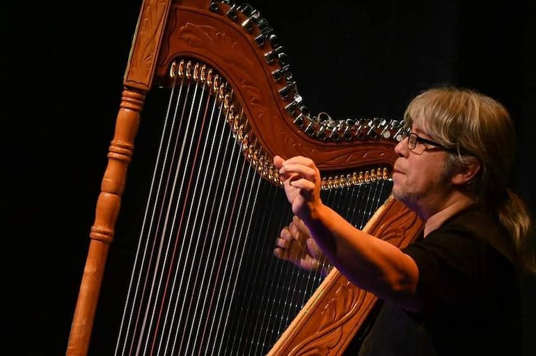 Ismael Ledesma toca el arpa en un ambiente de concierto oscuro.