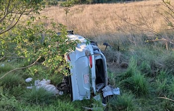 Vehículo volcado en un área rural, rodeado de pasto alto y vegetación. No hay personas visibles.