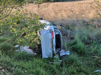 Vehículo volcado en un área rural, rodeado de pasto alto y vegetación. No hay personas visibles.