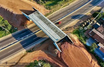 Vista aérea de una obra en construcción sobre carretera con vegetación y viviendas adyacentes.