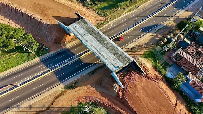 Vista aérea de una obra en construcción sobre carretera con vegetación y viviendas adyacentes.