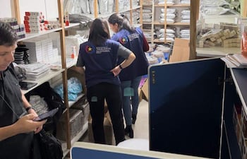 Dos mujeres con chalecos de Vigilancia Sanitaria revisan estantes mientras un hombre usa su teléfono móvil.