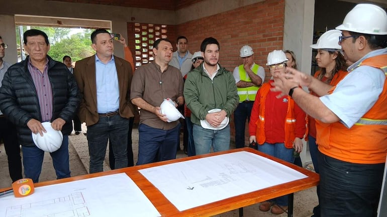 Walter Gutiérrez y Richard Ramírez en chaquetas conversan sobre planos en un entorno de construcción con ladrillos expuestos.