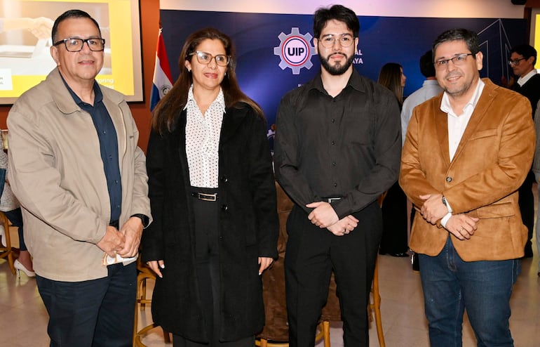 Cuatro personas posan en un salón: hombre con gafas y camisa oscura, otro en saco marrón, mujer en blusa blanca y abrigo negro, joven con barba.