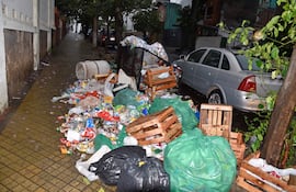 Basura acumulada en calle húmeda, con contenedor volcado y bolsas plásticas alrededor en Teodoro S Mongelos y 22 de Setiembre