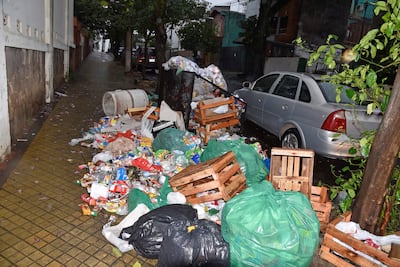 Basura acumulada en calle húmeda, con contenedor volcado y bolsas plásticas alrededor en Teodoro S Mongelos y 22 de Setiembre