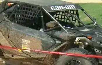 Un vehículo Can-Am negro cubierto de barro, en un área con césped y cinta de precaución roja.