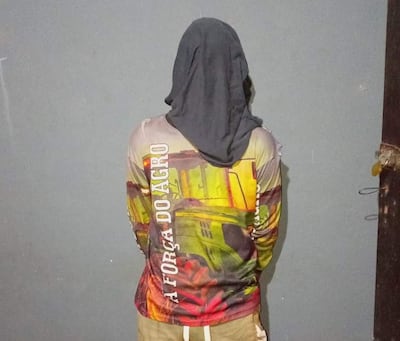 Persona con sudadera y paño oscuro en la cabeza, vista de espaldas, en interior con pared gris.