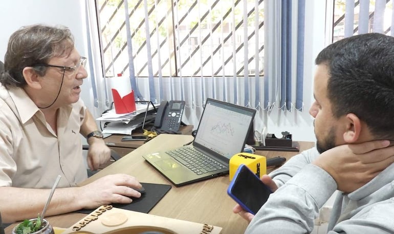 Jorge A. Sánchez, con camisa clara y gafas, gesticula frente a laptop mientras su colega lo escucha por atento.