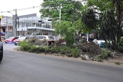 Escena urbana en Asunción con desechos y ramas en la calle, edificio moderno al fondo, sin personas presentes.