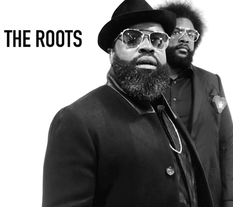 Dos hombres con barbas prominentes, uno con sombrero negro y gafas oscuras, luciendo un ambiente musical en fondo blanco.