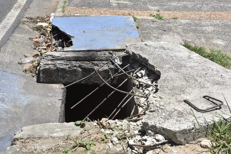 Gran agujero en acera de cemento, con varillas de metal expuestas y residuos alrededor.