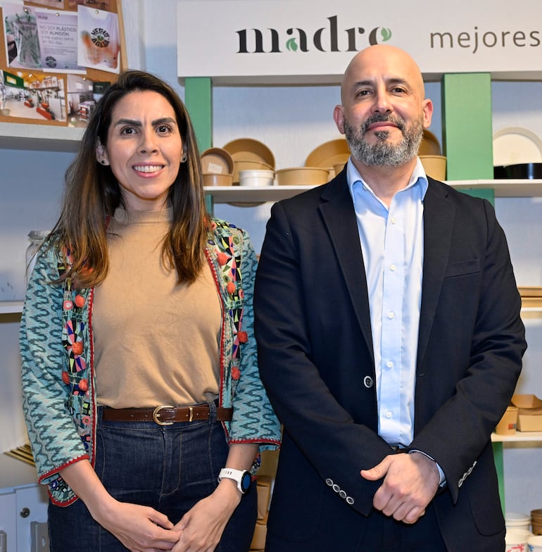 Jorge Daniel Duarte en chaqueta oscura sonríe junto a una mujer con abrigo decorado, en ambiente formal y neutral.