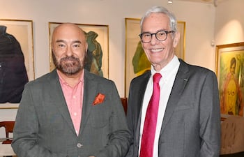 Dos hombres sonrientes en un entorno elegante: uno con saco gris oscuro y el otro en traje gris con corbata roja.