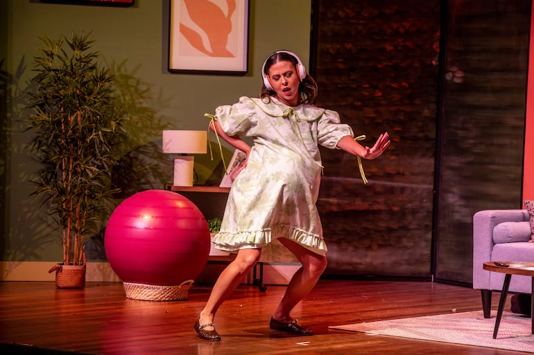 Mujer con vestido vintage floral y auriculares, sonriendo y bailando en un escenario minimalista con decoración verde.