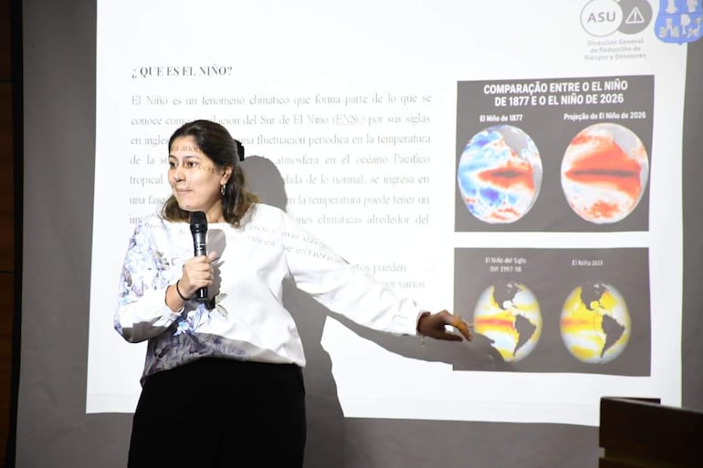 Mujer señalando proyección sobre El Niño, con expresión concentrada, en un aula con fondo neutro.
