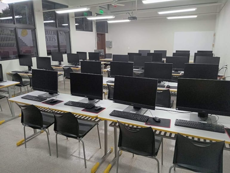 Aula de computación con 20 estaciones de trabajo, bien iluminadas y sin personas presentes.