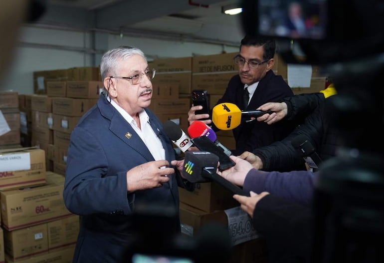 Isaías Ricardo Fretes, hombre mayor con gafas y saco oscuro, habla ante periodistas en un entorno cerrado lleno de cajas.