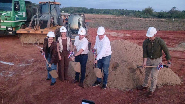 Adriana Ortiz Semidei y otros en ceremonia de colocación de primera piedra, todos con cascos y palas en un terreno de tierra roja.