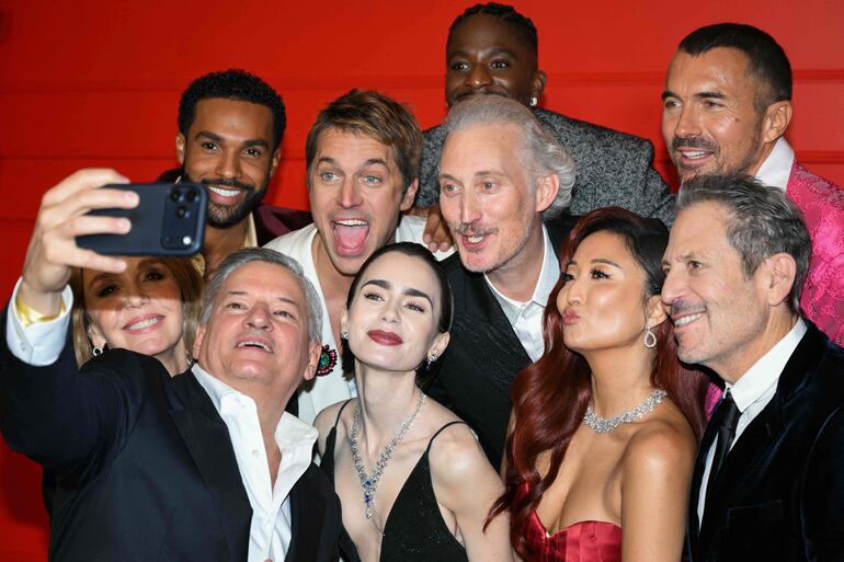 El director ejecutivo de Netflix, Ted Sarandos, se toma una selfie con la actriz francesa Philippine Leroy-Beaulieu, el actor británico Lucien Laviscount, el actor francés Lucas Bravo, la actriz estadounidense Lily Collins, el actor francés Bruno Gouery, el actor francés Samuel Arnold, la actriz estadounidense Ashley Park, el director, productor y guionista estadounidense Darren Star y el actor francés William Abadie durante el preestreno de la quinta temporada de la serie de televisión "Emily en París", en el Grand Rex, en París. (Blanca CRUZ / AFP)