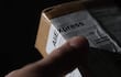 Mano sosteniendo un paquete de AliExpress con fondo negro, en un ambiente cerrado y con iluminación tenue.
