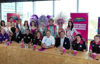 Mujeres con trajes de carnaval en el centro, mientras hombres en una mesa discuten el evento con entusiasmo.