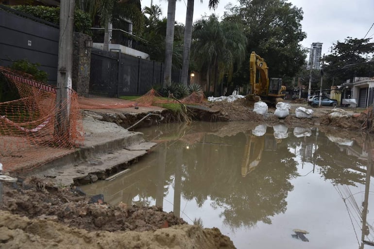 Gran bache lleno de agua en Santo Domingo, con excavadora amarilla trabajando y bolsas de arena cercanas a la obra.
