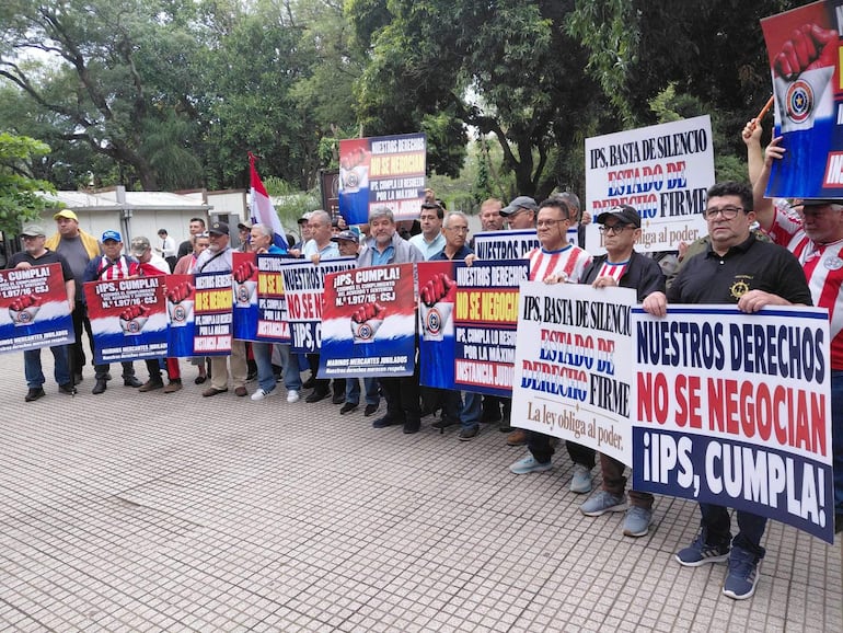 Veinte personas sostienen pancartas en la Plaza de la Justicia, algunos lucen camisetas a rayas del Club Olimpia.