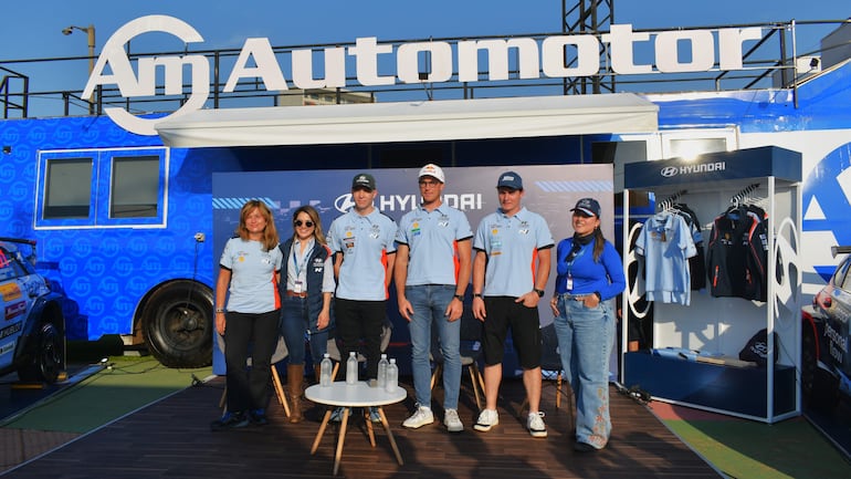 Cuatro hombres y dos mujeres del equipo Hyundai, todos con camisetas celestes y naranjas, conversan en un evento al aire libre.