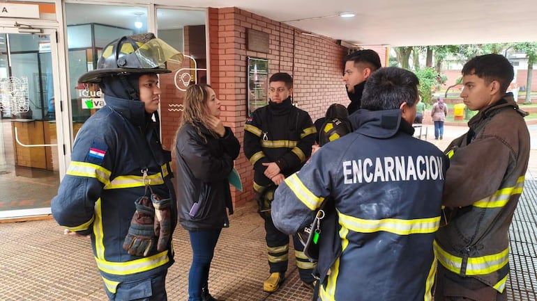 Bomberos en uniforme de Encarnación discuten, una mujer conversa con ellos mientras sostienen la bandera paraguaya.
