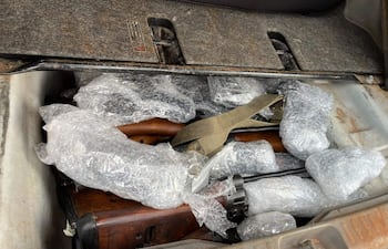Rifles envueltos en plástico burbuja dentro de un maletero de vehículo desgastado, sin personas visibles.