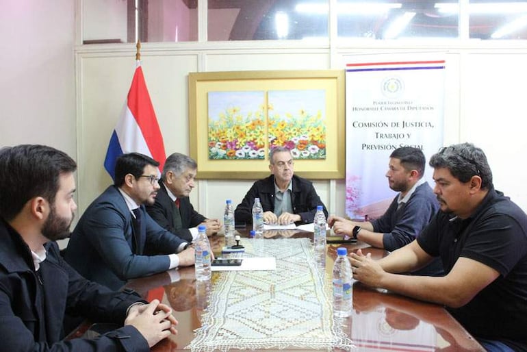 Reunión con Yamil Esgaib y otros hombres sentados alrededor de una mesa en un ambiente formal, con bandera de Paraguay atrás.