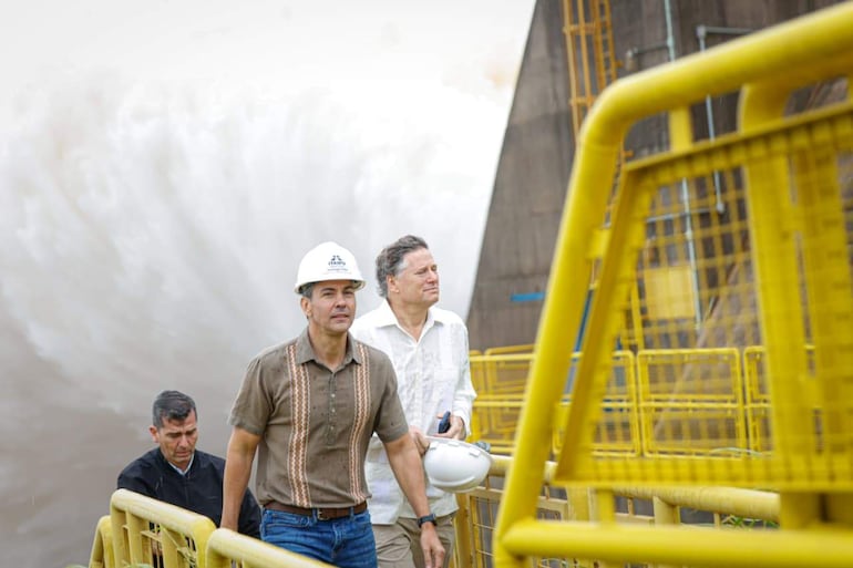 Santiago Peña con camiseta clara y sombrero blanco lidera la visita, rodeado de dos hombres en entorno industrial con grandes estructuras de metal.