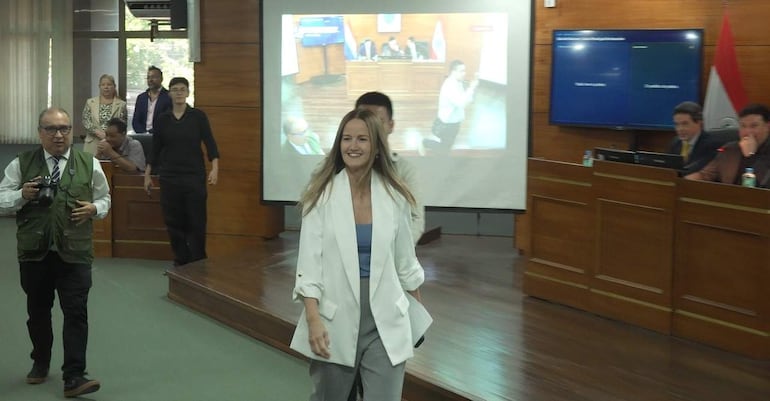Soledad Núñez con blazer blanco y blusa azul, sonriente, en reunión con otros asistentes en ambiente formal.