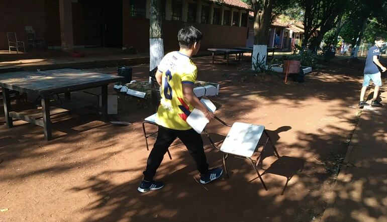 Un alumno lleva las últimas sillas disponibles y que no tienen para colocar los cuadernos.