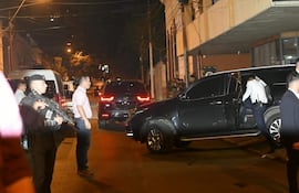 Hombre de traje oscuro subiendo a una SUV negra, acompañado de personal de seguridad y vigilancia en una calle iluminada.