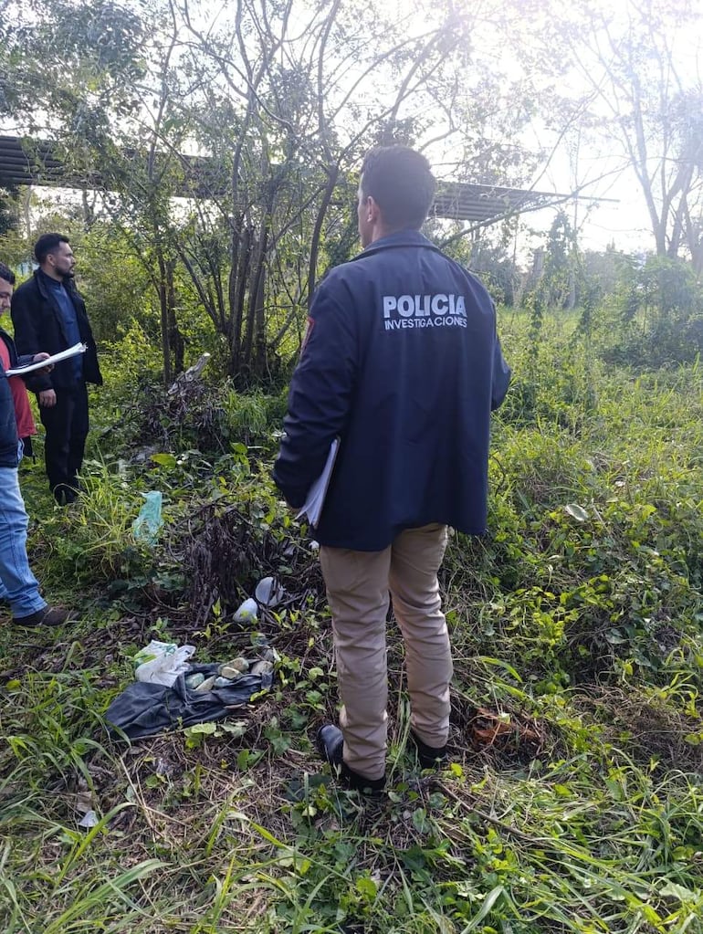 Hombre de espaldas con chaqueta de policía, tomando notas en una escena rural con vegetación densa.