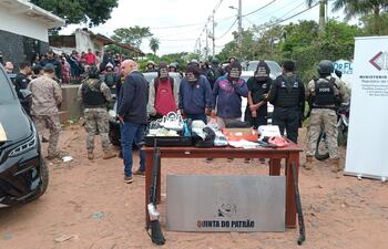 Cuatro detenidos con capuchas en la cabeza, parados detrás de una mesa donde se exhibe parte de lo incautado en el procedimiento