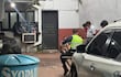 Hombre policía con chaleco verde observa a tres hombres sentados en el suelo, rodeados de un ambiente desordenado.