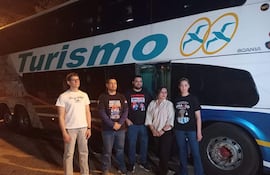 Cinco personas, cuatro hombres y una mujer, frente a un autobús iluminado, visten camisetas de sindicato y camisa a rayas.