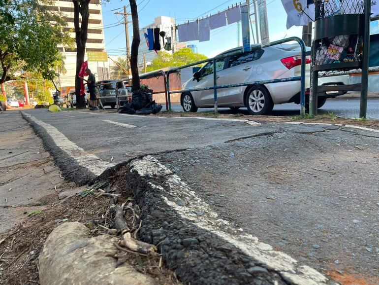 Hombre de pie en acera con prenda roja, rodeado de coches estacionados en una calle urbana de Asunción.