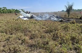 Bomberos en ropa de emergencia extinguiendo incendios alrededor de una aeronave destrozada, en un campo abierto bajo un cielo despejado.