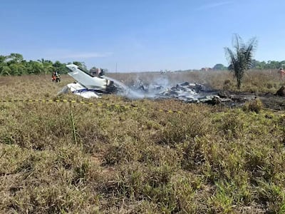 Bomberos en ropa de emergencia extinguiendo incendios alrededor de una aeronave destrozada, en un campo abierto bajo un cielo despejado.