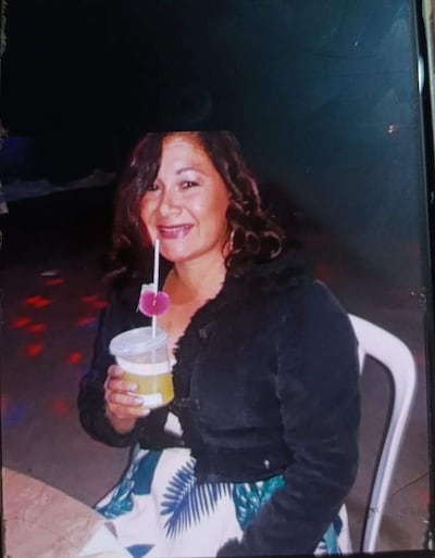 Mujer con cabello rizado y chaqueta negra sonríe sosteniendo un vaso, en ambiente con luces de colores.