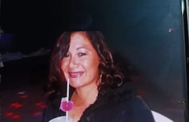 Mujer con cabello rizado y chaqueta negra sonríe sosteniendo un vaso, en ambiente con luces de colores.