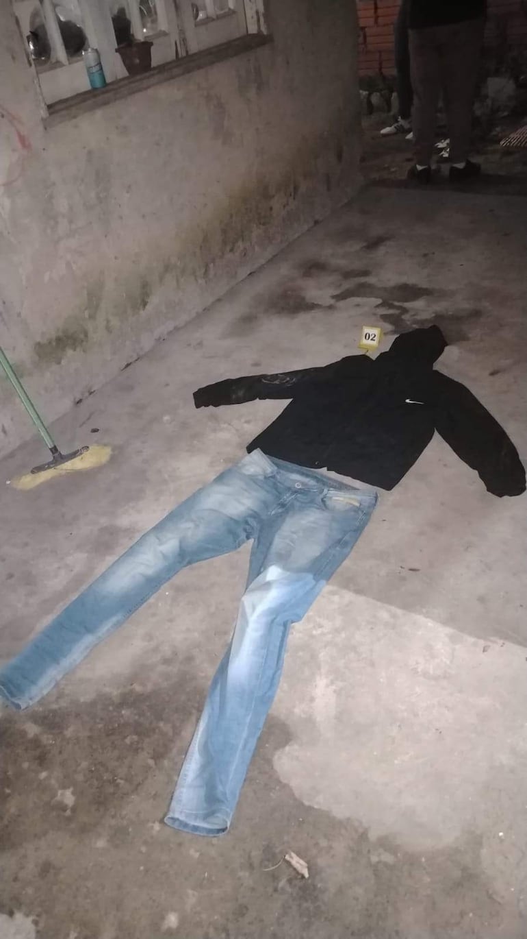 Chaqueta negra y jeans azules en el suelo de un ambiente desordenado, con placa numerada cerca como evidencia.