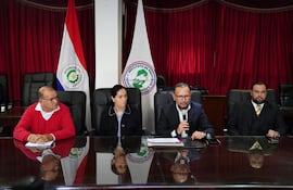 Pablo José Morinigo Cáceres, Walter Laguardia y Derlis León en mesa con banderas del IPS y Paraguay, expresiones tranquilas en ambiente formal.